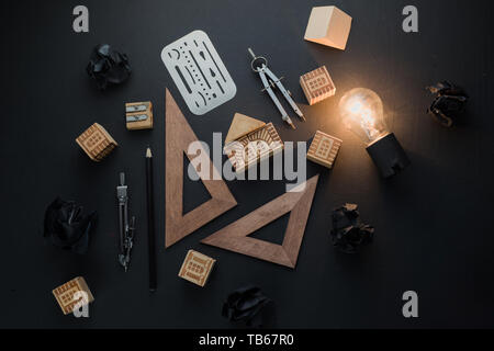 L'innovation et la créativité concept pour l'ingénierie et la science. Ampoule Lumière brillant dans le noir sur noir mise à plat avec des boules de papier froissé et des crayons. Banque D'Images