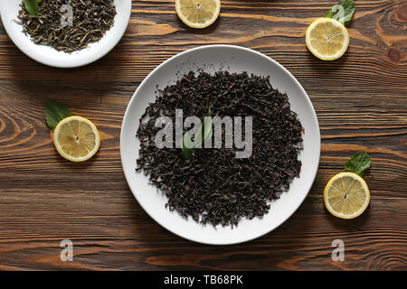 Plaques avec différents types de sécher les feuilles de thé et les tranches de citron sur la table en bois Banque D'Images