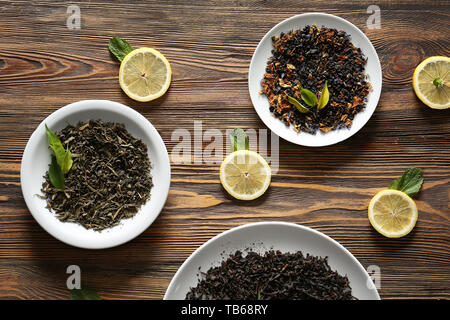 Plaques avec différents types de sécher les feuilles de thé et les tranches de citron sur la table en bois Banque D'Images