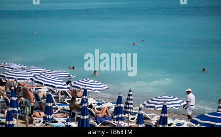 Mer avec parasols rayé bleu et blanc et des chaises de plage à Nice, dans la Riviera française. Banque D'Images