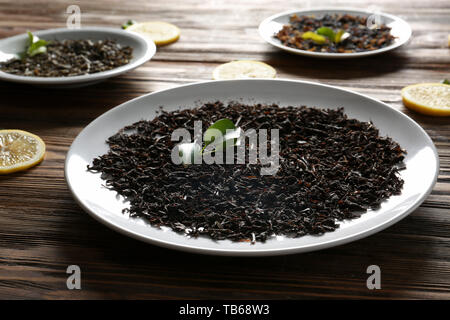 Plaques avec différents types de sécher les feuilles de thé et les tranches de citron sur la table en bois Banque D'Images
