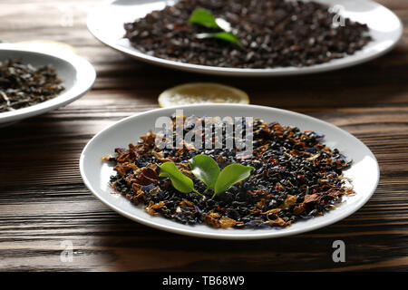 Plaques avec différents types de sécher les feuilles de thé et les tranches de citron sur la table en bois Banque D'Images