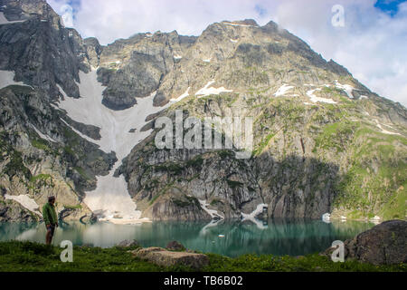 Gadsar, Cachemire, Inde- du- 18 mai 2019 : Un randonneur surplombant la mer bleue turquoise des eaux du lac Gadsar avec la source glacier dans l'arrière-plan. G Banque D'Images