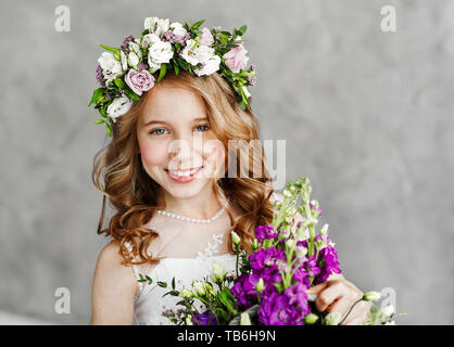 Close-up portrait of cute little girl dans une gerbe de fleurs sur la tête et un panier de belles fleurs de printemps. Banque D'Images