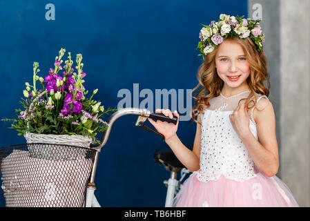 Close-up portrait of cute little girl dans une gerbe de fleurs sur la tête et un panier de belles fleurs de printemps. Banque D'Images