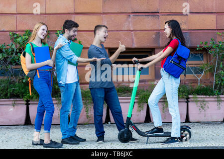 Jeune femme avec scooter électrique rencontrer des amis dans la ville de plein air Banque D'Images