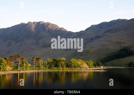 Réflexions du soleil au lac Buttermere avec meules de foin à l'arrière-plan de prendre le dernier de la soirée soleil sur les collines du Lake District, Banque D'Images
