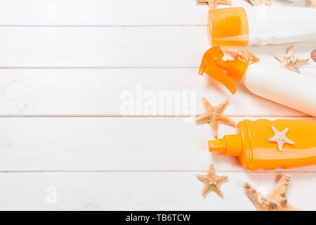 Bouteilles d'écran solaire avec les coquillages sur la table en bois blanc. Accessoires voyages santé vue d'en haut. Banque D'Images