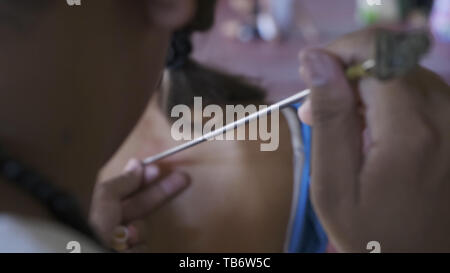 Yantra tatouage ou sak yant, tatouage sacré thaïlandais. master dessine une fille tatouage Sak Yant incolore avec une huile spéciale. La Thaïlande. Banque D'Images