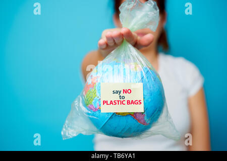 Femme tient en mains le sac en plastique avec texte autocollant dire non aux sacs en plastique et de la planète terre à fond bleu. Le concept de la pollution plastique. Banque D'Images