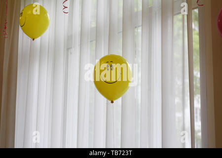 Ballon jaune avec un sourire. Smiley - un symbole de bonheur et de joie. Ballon gonflable sur l'arrière-plan de la fenêtre. Banque D'Images