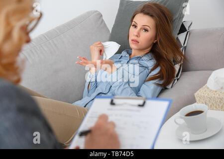 Femme d'âge moyen avec thérapie psychologyst allongé sur le canapé à la clientèle au bureau de prendre des notes pendant que son histoire de fille tissu holding émotionnelle Banque D'Images