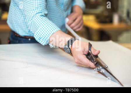 Adapter les coupes tendance marquée sur le tissu avec de grands ciseaux sur l'établi dans sa boutique, vue en gros plan de ses mains . Banque D'Images