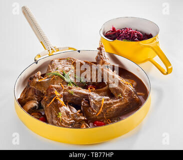 Des portions de lapin sauvage rôti parfumé au zeste d'orange, fines herbes et champignons servi dans une sauce riche dans une casserole jaune rouge avec accompagnement de Banque D'Images