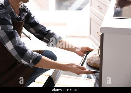 Jeune homme de prendre du pain frais hors de four dans la cuisine Banque D'Images