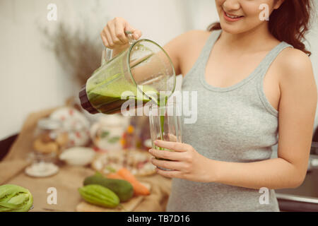 Happy woman pouring un cocktail vert dans une tasse au cours de régime de detox Banque D'Images