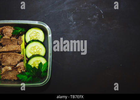 Boeuf bouilli et des morceaux de concombre dans un petit récipient sur un fond noir, vue du dessus, Close up. L'alimentation saine, l'alimentation, l'espace de remise en forme. copie. Banque D'Images