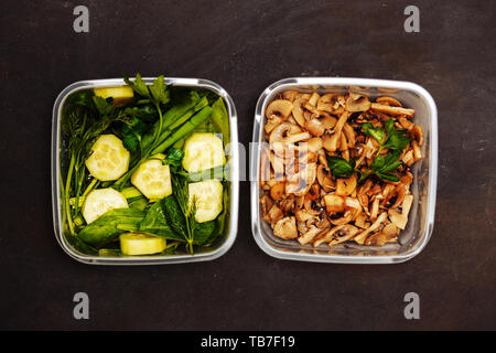 Mise à plat de deux conteneurs avec les légumes et les champignons sur un fond en bois noir, gros plan. Régime alimentaire sain, une bonne nutrition des concepts. Banque D'Images