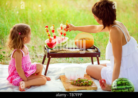 Deux filles sourire mange tranche de melon d'eau à l'extérieur sur pré. Mère et fille passent du temps ensemble. Régime alimentaire, vitamines, concept d'aliments sains. Banque D'Images