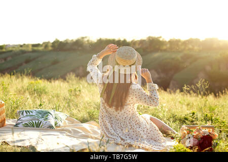 Femme heureuse vie, belle fille détendue dans un chapeau de paille sur la nature de l'arrière sur pique-nique - camping. Banque D'Images