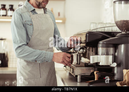 Coffee shop. Beau barbu holding cruche de lait et mousse de lait pour une tasse de Cappuccino. Banque D'Images