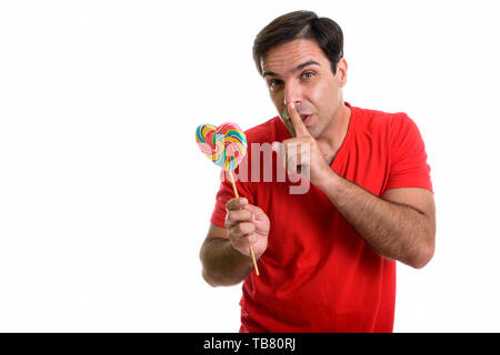 Portrait of young man holding Persique sucette en forme de coeur avec le doigt sur les lèvres contre isolé sur fond blanc Banque D'Images