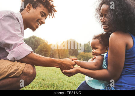 Happy African family enjoying moment ensemble dans un parc public - La mère et le père s'amusant à jouer avec leur fille en plein air au coucher du soleil Banque D'Images