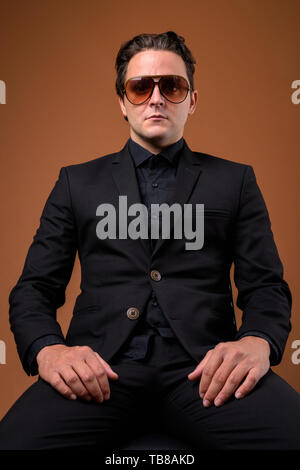 Studio shot of Italian businessman wearing costume noir contre fond brun Banque D'Images