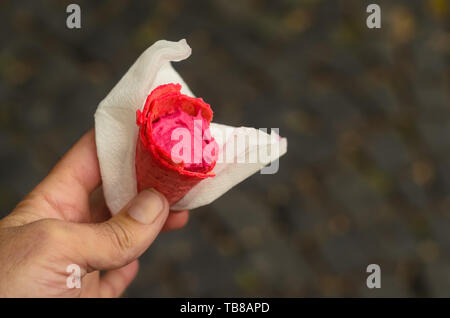 Un homme tenant un cornet de crème glacée framboise dans un linge dans la rue. Cornet de crème glacée est partiellement mangés Banque D'Images