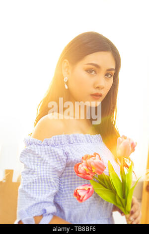 Belles femmes asiatiques en robe bleue avec des jacinthes roses dans les mains avec du soleil le matin à partir de la fenêtre . Banque D'Images