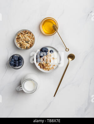 Porridge avec des écrous, des yaourts, des bleuets, du miel avec du miel stick, avec la table d'or sur fond de marbre blanc. L'espace de copie de texte, de la mise à plat Banque D'Images