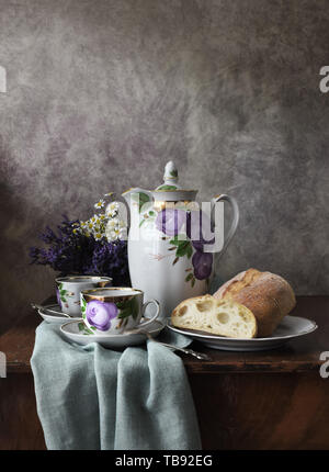 Retro still life poster petit-déjeuner. Vintage coffee pot électrique tasses, cuillère en argent, du pain de la boulangerie. Lumière sombre, table en bois, , tissu Banque D'Images
