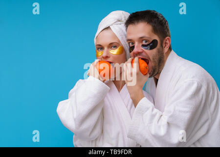 Photo de l'homme et de la femme avec les blocs de gel sous les yeux et en robe blanche de mordre les oranges Banque D'Images