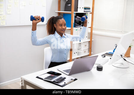 Smiling Young Woman Exercising With Dumbbells bleu Banque D'Images