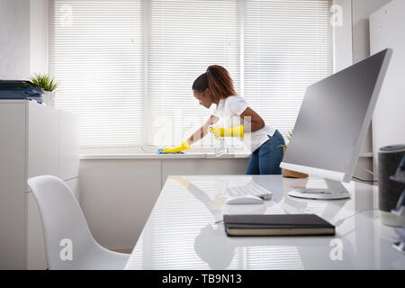 Jeune femme Nettoyage de l'appui de fenêtre avec serviette et bouteille de Jet In Office Banque D'Images