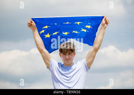 Jeune adulte caucasien homme tenant sur une plage, tenant le drapeau de l'Union européenne Banque D'Images