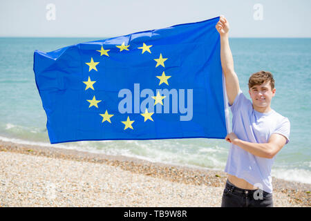 Jeune adulte caucasien homme tenant sur une plage, tenant le drapeau de l'Union européenne Banque D'Images