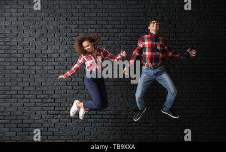 Jeune couple de saut de fond brique sombre contre Banque D'Images