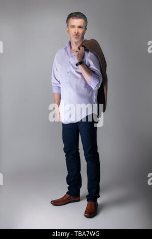 Middle aged businessman wearing business tenue décontractée. L'homme se posant avec untucked shirt à manches longues avec des jeans et tenant une veste. Montre m Banque D'Images