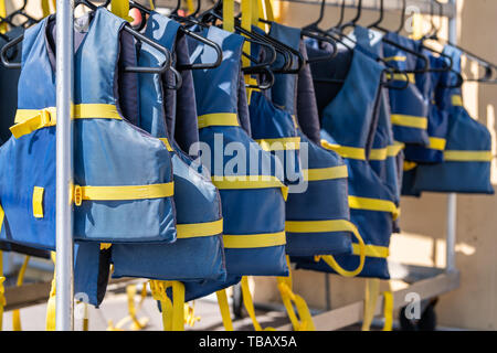 Pile de pendaison bleu et jaune gilets sur des cintres à l'extérieur, à l'extérieur dans le soleil, des vêtements de sécurité pour bateaux de location au magasin ou boutique Banque D'Images