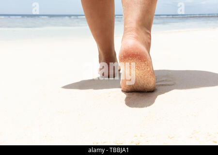 La section basse de Woman's pieds marchant sur une plage de sable vers la mer Banque D'Images