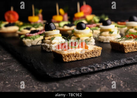 Plaque en ardoise avec de savoureux canapés sur tableau noir, gros plan Banque D'Images