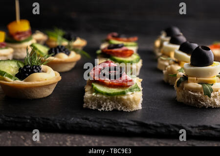 Plaque en ardoise avec de savoureux canapés sur tableau noir, gros plan Banque D'Images