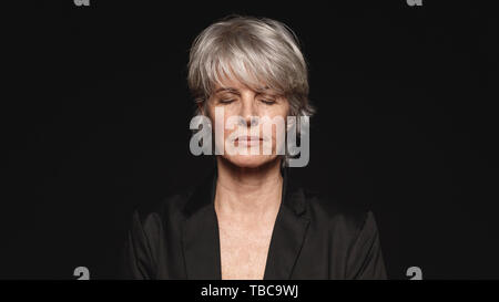 Close up of senior woman avec les yeux fermés. Femme dans l'usure formelle isolé sur fond noir. Banque D'Images