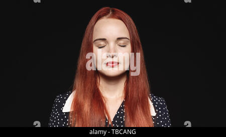 Portrait d'une femme avec de longs cheveux brun rouge isolé sur fond noir. Gros plan d'une femme avec les yeux fermés. Banque D'Images