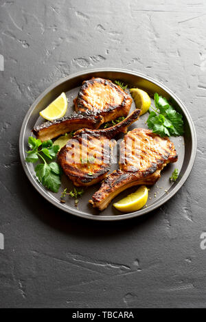 Steaks de porc grillé avec des greens et citron sur plaque sur fond noir en noir. Banque D'Images