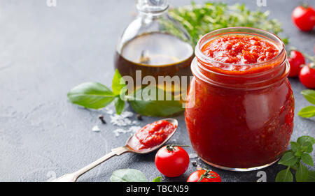 Sauce tomate traditionnelle dans un bocal en verre avec des herbes fraîches, les tomates et l'huile d'olive. Copier l'espace. Fond d'ardoise. Banque D'Images