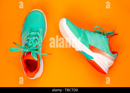 Cyan, rouge, blanc paire de chaussures de tennis en studio shot sur fond orange. Directement à partir de ci-dessus. Banque D'Images