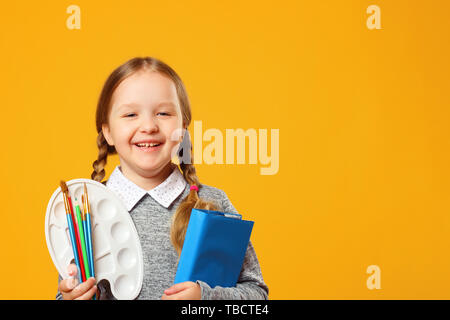 Portrait d'une petite fille sur un fond jaune. Lycéenne tient un livre, crayons, pinceaux et une palette. Le concept de l'éducation. Spa de copie Banque D'Images