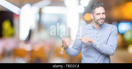 Jeune homme séduisant sur fond isolé en pointant sur l'arrière derrière avec la main et Thumbs up, souriant confiant Banque D'Images